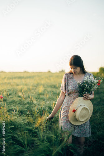 Wallpaper Mural Beautiful woman with wildflowers and straw hat walking in barley field in sunset light. Stylish female relaxing in evening summer countryside and gathering flowers. Atmospheric tranquil moment Torontodigital.ca