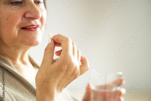 Close up of a retired woman in casual clothes at home holding pill and glass water. 