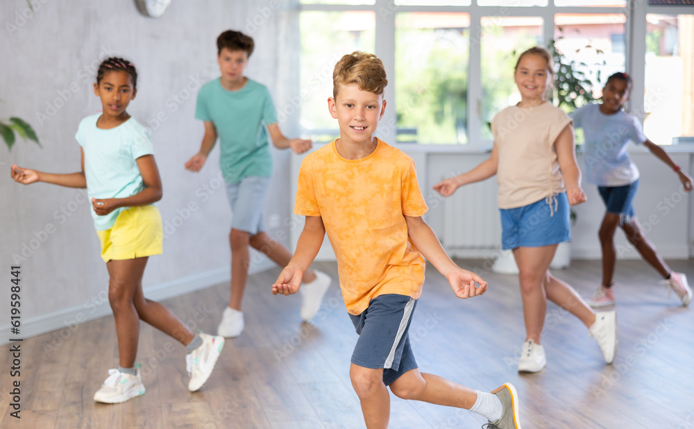 Man child performs movements during warm-up, limbering-up part of workout together with peers. Group of young girls and guys dance modern hip hop in fitness club unfocused
