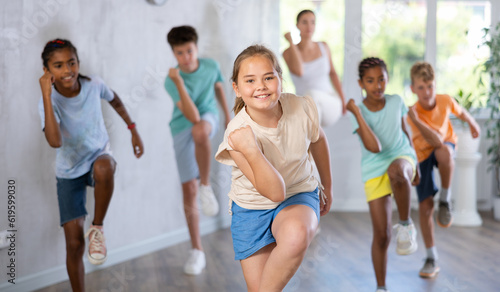 Energetic happy tween girl practicing modern vigorous movements in dance class with group of children..