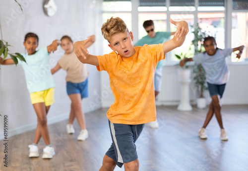 Positive juvenile boy engaged in Breakdancing together with children's group in training room during workout session