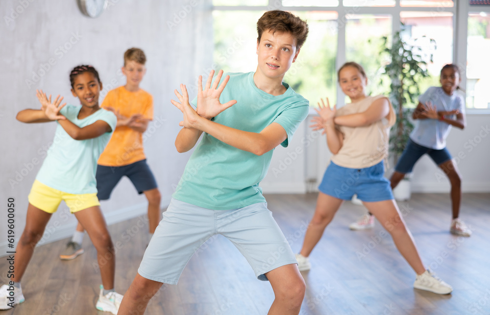 Fototapeta premium Positive boy exercising in group of classmates during dance class at dance studio