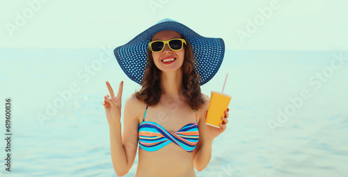 Summer vacation, beautiful happy smiling woman with cup of juice wearing straw hat, sunglasses on the beach on sea coast background