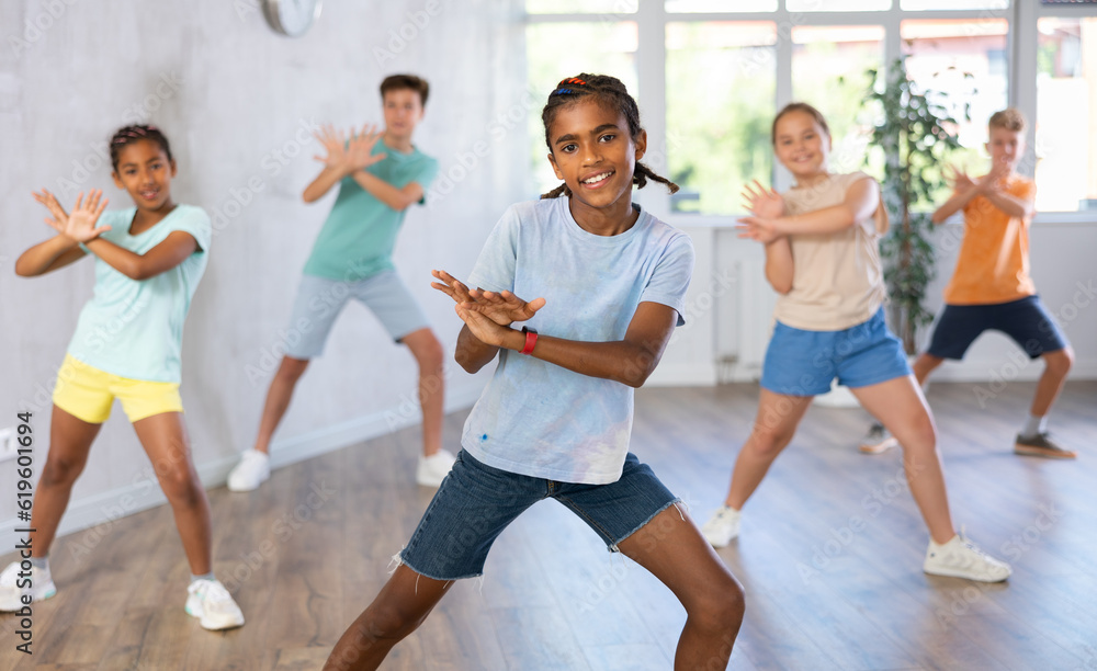 Fototapeta premium Smiling african american preteen boy dancer practicing active vigorous dance with group in modern studio..