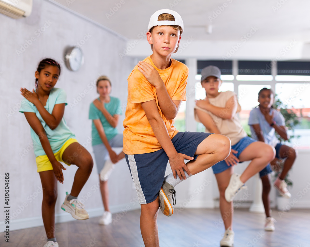 Fototapeta premium Dynamic little boy training Break-dance poses in dancehall with other attendees of dancing courses