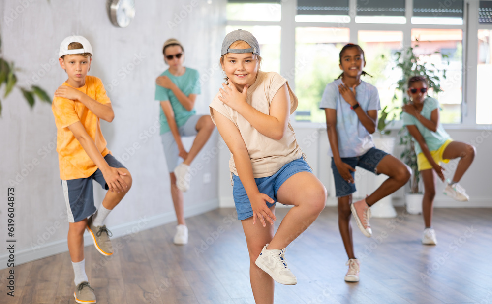 Fototapeta premium Portrait of cheerful preteen girl enjoying modern dancing during group training in dance studio, practicing hip-hop movements..