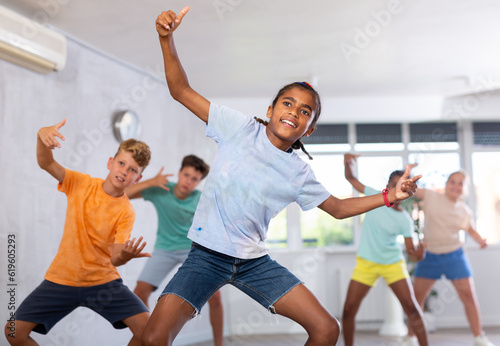 African boy performs movements during warm-up, limbering-up part of workout together with peers. Group of young girls and guys dance modern waacking in fitness club unfocused photo