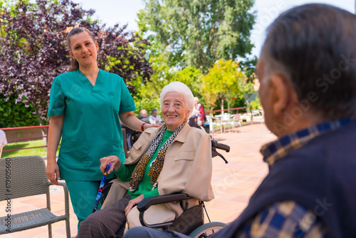 Portrait of an elderly woman with the nurse in the wheelchair in the garden of a nursing home or retirement home © unai