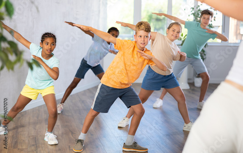 Emotional cheerful tween boy enjoying contemporary dance with group of children, showcasing dabbing move..