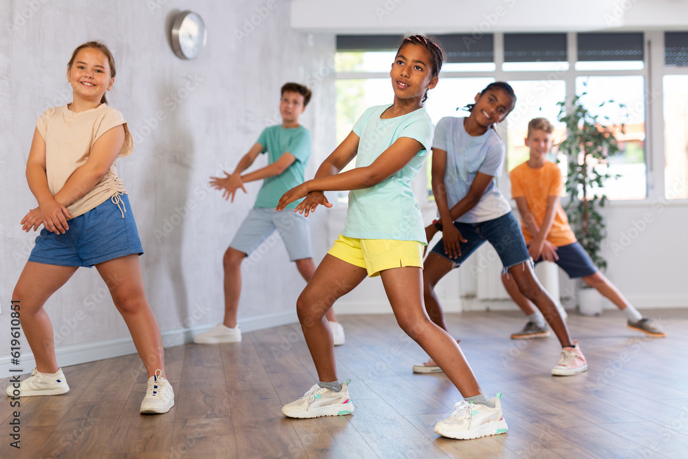 Portrait of cheerful preteen african american girl enjoying active dancing during group training in dance studio..