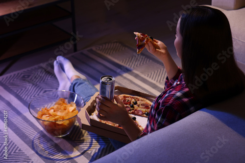 Young woman eating pizza while watching TV in room at night. Bad habit photo