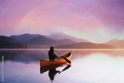 USA, St. Armand, Rear view of woman canoeing on calm Lake Placid at sunset in Adirondack Park photo