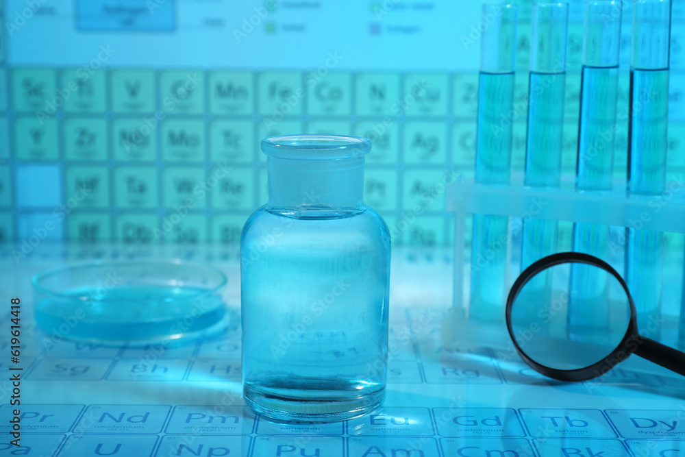 Laboratory glassware, petri dish and magnifying glass on periodic table of elements, closeup. Color tone effect Laboratory glassware, petri dish and magnifying glass on periodic table of elements, closeup. Color tone effect