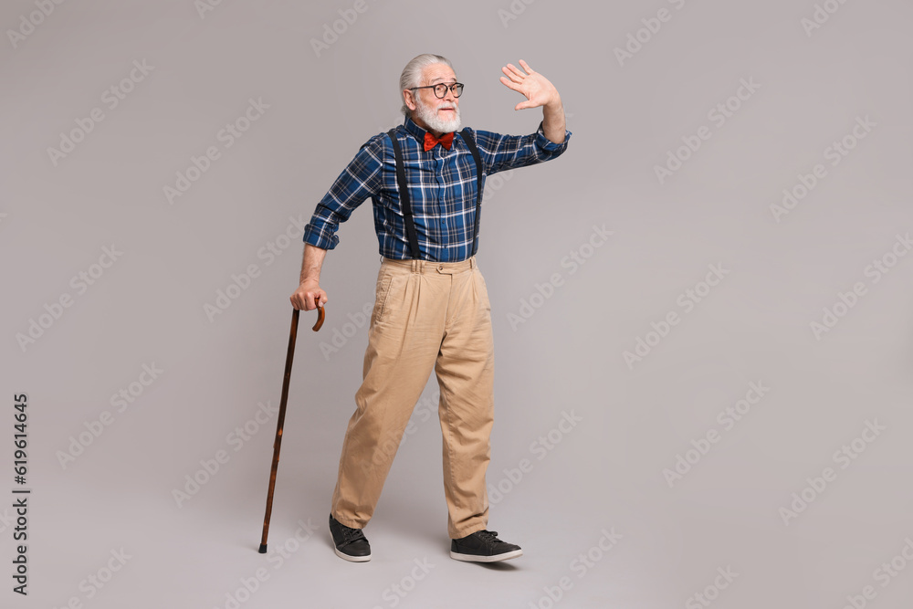 Senior man with walking cane waving on gray background Senior man with walking cane waving on gray background