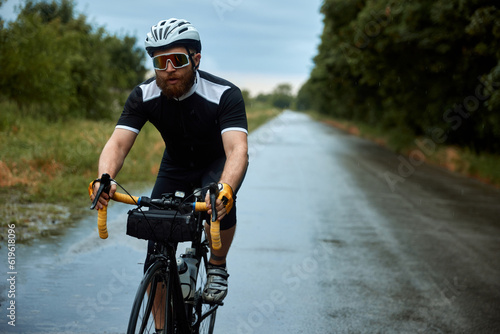 Concentrated, young, bearded man, cyclist in uniform, helmet and glasses riding bike on road in chill evening. Concept of sport, hobby, leisure activity, training, health, speed, endurance, ad