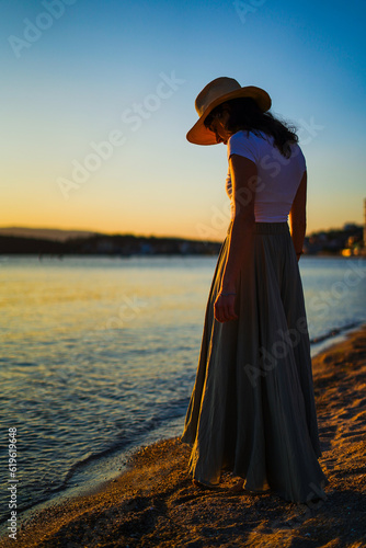 Girl with straw hat looking at the sea on the sunset on the beach