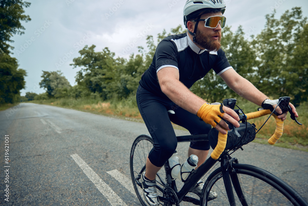 Sportsman, bearded man, cyclist in helmet, glasses and uniform riding bike on wet road in cloudy chill evening. Forest ride. Concept of sport, hobby, leisure activity, health, speed, endurance, ad Sportsman, bearded man, cyclist in helmet, glasses and uniform riding bike on wet road in cloudy chill evening. Forest ride. Concept of sport, hobby, leisure activity, health, speed, endurance, ad