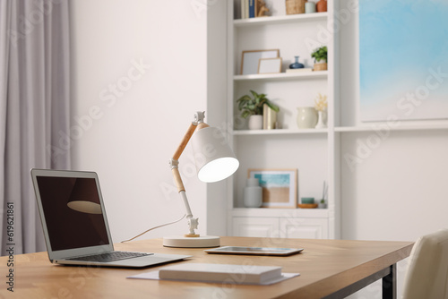 Interior design. Cosy workplace with laptop and lamp on wooden table © New Africa