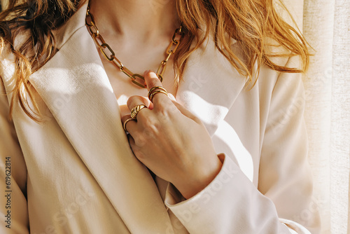 Close-up of female hand with rings touching her golden chain necklace, natural light