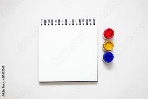 Caderno argolado com folhas brancas, e potes de guache nas cores primárias photo