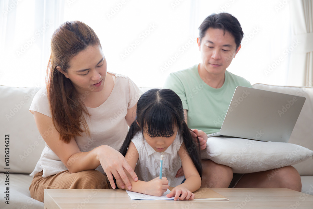 Happy family with mother teaching homework with daughter and father working with laptop on sofa in living room at home, mom explaining schoolwork with kid together, lifestyles and education. Happy family with mother teaching homework with daughter and father working with laptop on sofa in living room at home, mom explaining schoolwork with kid together, lifestyles and education.