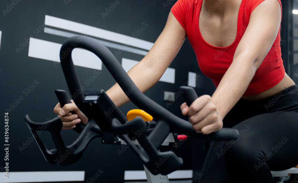 Young asian woman riding bicycle machine for workout training in fitness gym club, female cycling for exercise with motivation and concentration for wellbeing and weightloss, sport and healthcare. Young asian woman riding bicycle machine for workout training in fitness gym club, female cycling for exercise with motivation and concentration for wellbeing and weightloss, sport and healthcare.