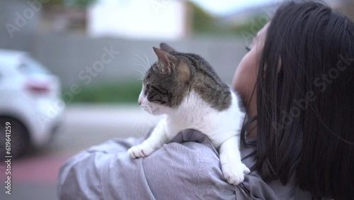 Scared cat being carried by woman's arms has fear to cars and road.