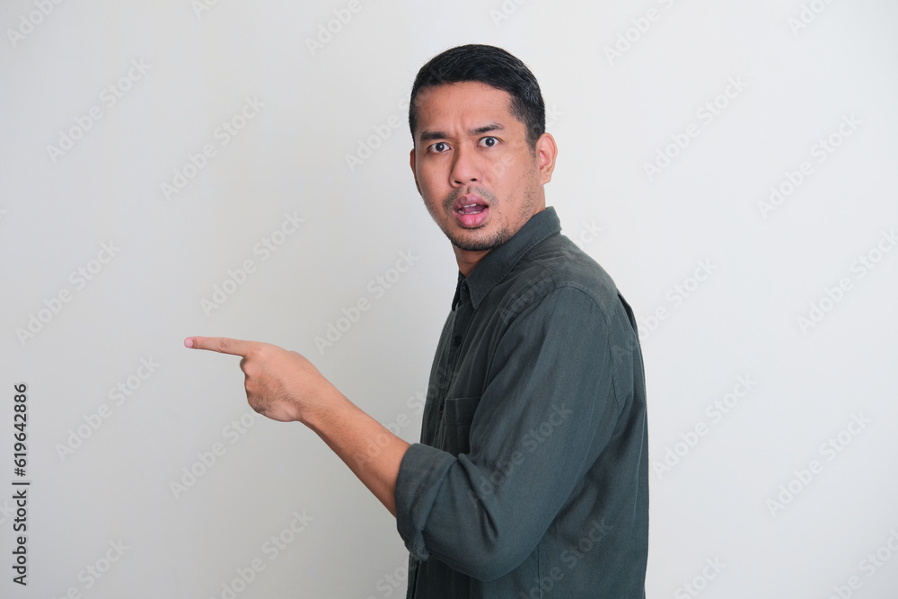 Side view of Asian man pointing to the left side with worried expression