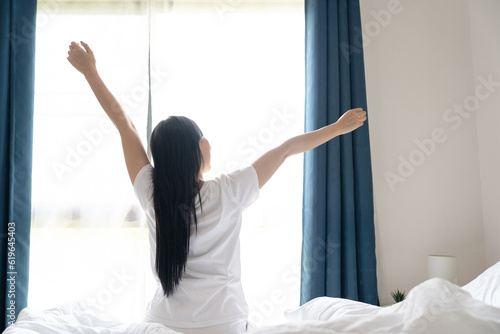 Young asian woman sitting on the bed and stretch oneself in the morning at home