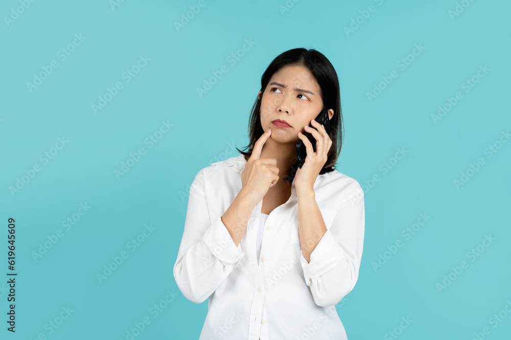 Asian woman hand holding smart phone wonder, thinking and planning something standing over green background. Asian woman hand holding smart phone wonder, thinking and planning something standing over green background.