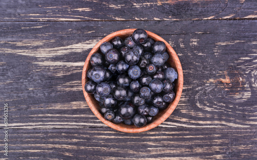 Bowl full of fresh blueberries on a wooden background top view
