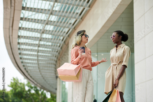 Stylish young women standing at shopping mall entrance and discussing news