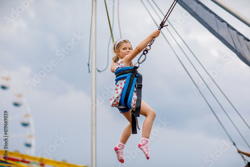 Little preschool girl enjoying jumping with trampoline jumping rope. Happy child in amusement park. Family activity