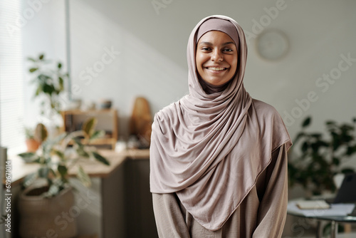 Photos Happy young Muslim woman in beige hijab standing in front of camera and looking