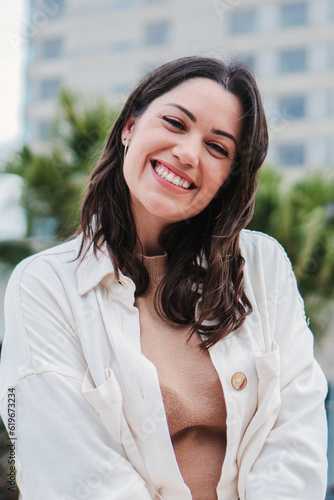 Vertical individual portrait of young adult woman smiling and looking at camera with white tooth standing outdoors. Front view of happy teenage girl with positive expression. Cheerful lady laughing