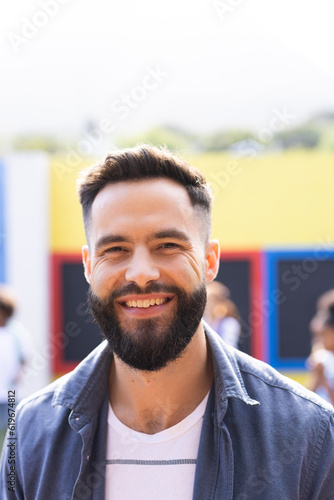 Vertical portrait of smiling, bearded caucasian male school teacher outdoors, with copy space