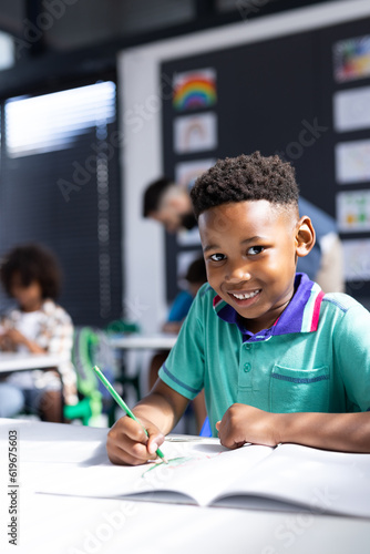 Vertical of happy african american schoolboy at desk in elementary school classroom, with copy space