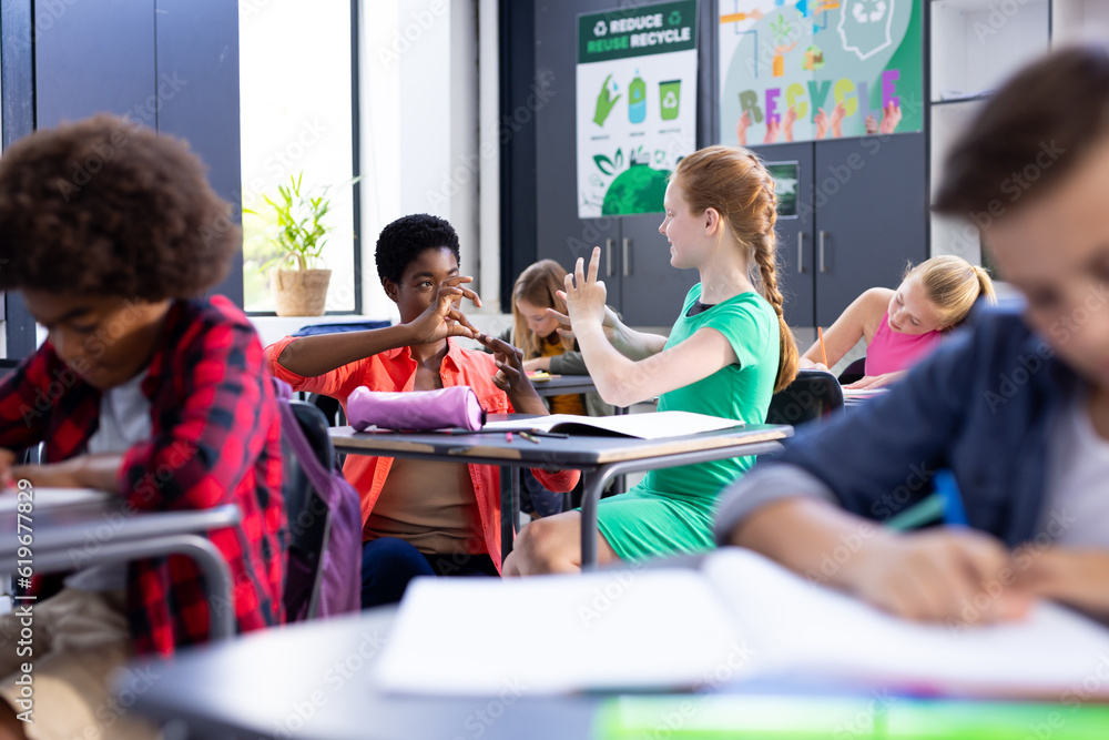 Happy, diverse female school teacher and schoolgirl practicing sign language in class Happy, diverse female school teacher and schoolgirl practicing sign language in class