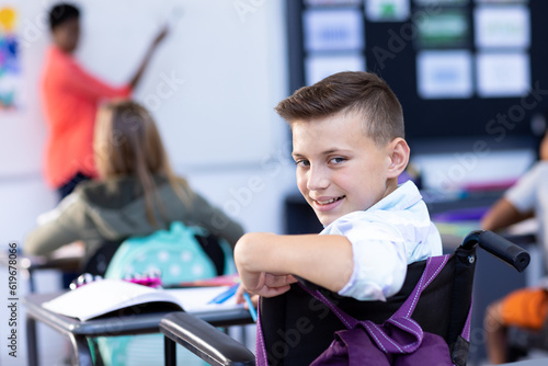 Portrait of smiling caucasian schoolboy turning round at desk in class