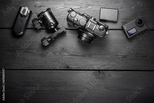 Digital compact and action cameras and equipment on black wooden plank table. top view.