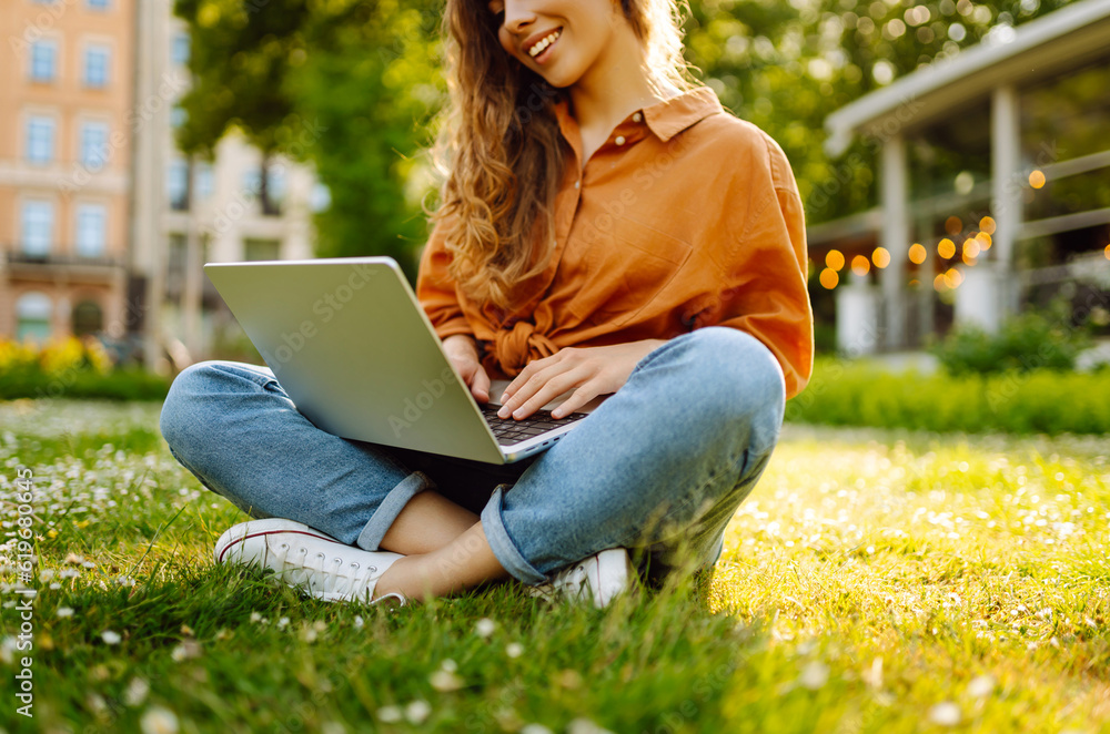 Beautiful female freelancer sits on a green meadow with a laptop. Online education. Happy woman running outdoors enjoying the sun. Freelancing concept. Beautiful female freelancer sits on a green meadow with a laptop. Online education. Happy woman running outdoors enjoying the sun. Freelancing concept.
