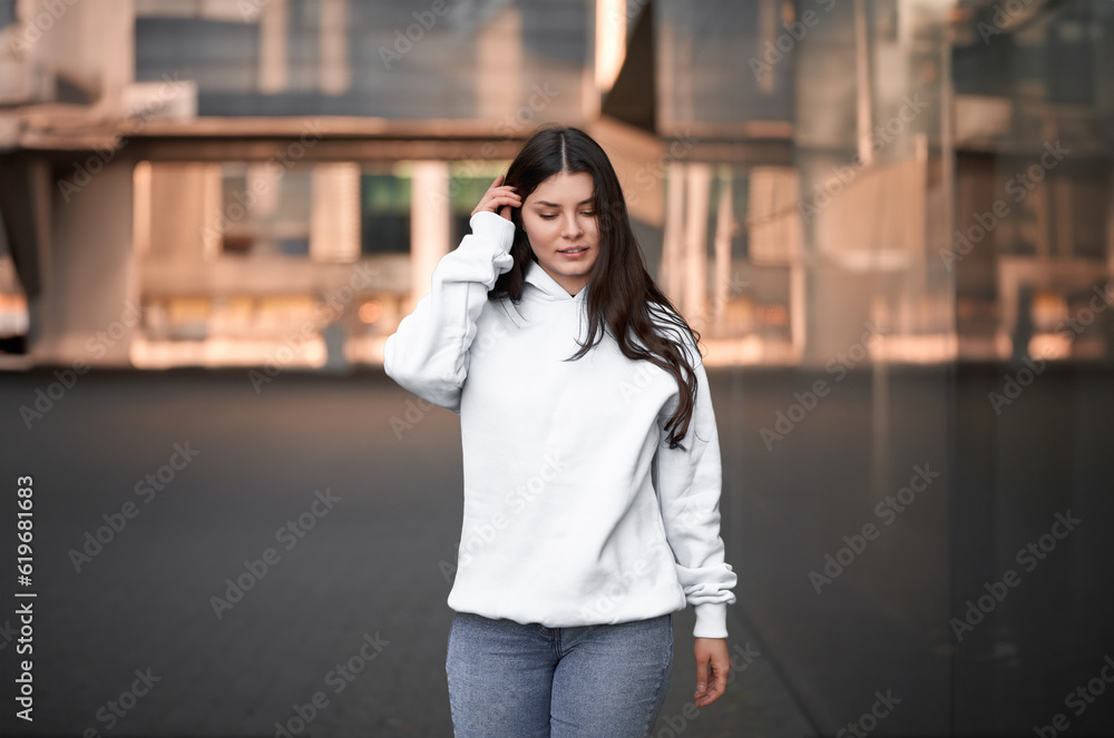 Fototapeta premium the woman wears a white hoodie. The empty space on her blouse is for logo design and branding clothing mockup. Basic sweatshirt template.