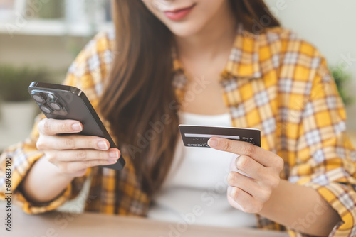 Bill pay, shopping order online internet asian young woman hand holding credit card and mobile smart phone on desk at home, female using banking service to secure payment with purchase on store.