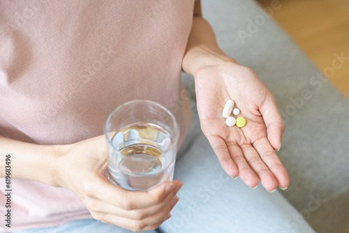 Sick, asian young woman, girl hand holding pill capsule, painkiller medicine from stomach pain, head ache, pain for treatment, take drug or vitamin and glass of water at home, pharmacy and health care © KMPZZZ