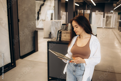 Happy brunette female interior designer choosing flooring tile color texture samples at store shop. Woman architect choice floor and wall finishing material for architecture and construction industry.