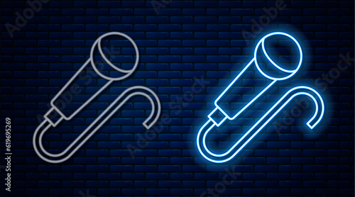 Glowing neon line Microphone icon isolated on brick wall background. On air radio mic microphone. Speaker sign. Vector