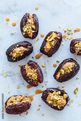 Dates stuffed with peanut butter and pistachios on white marble background. Healthy vegan dessert, snack recipe.