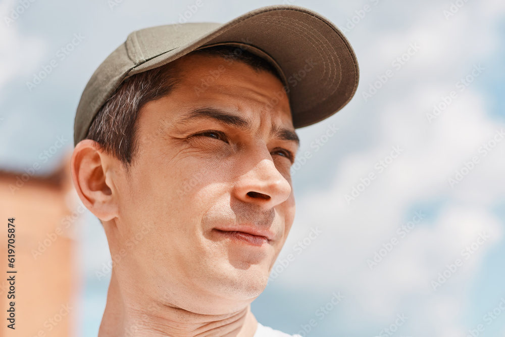 Young man posing on background of clear sky wearing baseball cap looking away with dreamy facial expression. Young man posing on background of clear sky wearing baseball cap looking away with dreamy facial expression.