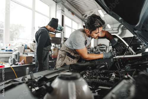 Two male mechanics repairing car in car service