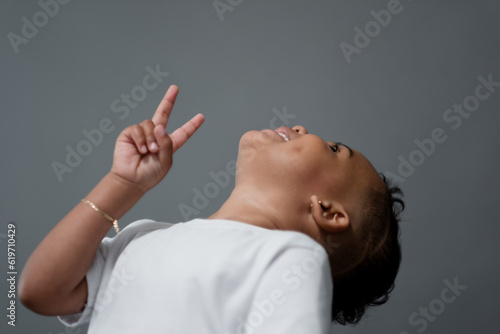 Throwing his head back in giggles, a toddler poses for a portrait and gives a two-fingered peace sign.